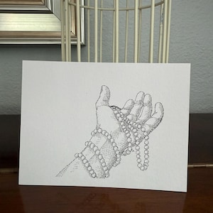Könnte beinhalten: Eine Schwarzweiß-Zeichnung einer Hand, die eine Perlenkette hält. Die Hand ist realistisch gezeichnet, mit den Fingern, die sich um die Perlen legen. Die Perlen sind in einer einfachen, runden Form gezeichnet.