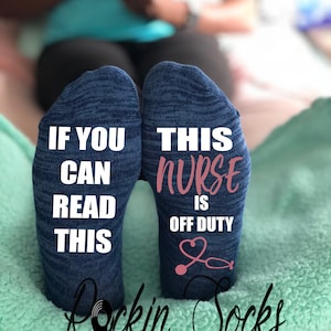 May include: A pair of blue socks with white text. One sock reads "If you can read this" and the other sock reads "This nurse is off duty". The socks have a pink stethoscope graphic and the words "Rockin Socks" are printed in black below the socks.