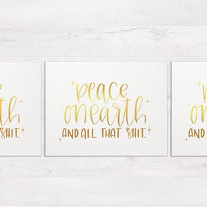 May include: Three gold foil prints with the text "peace on earth and all that shit." on a white background.
