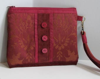 May include: A burgundy clutch bag with a gold chain strap and three red buttons. The bag has a floral pattern.