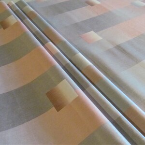 May include: A close-up of a fabric with a geometric pattern of horizontal stripes in shades of gray, pink, and white. The fabric is folded in half, showing the pattern on both sides.