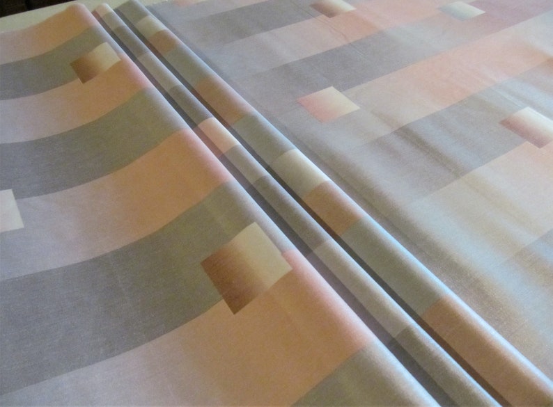 May include: A close-up of a fabric with a geometric pattern of horizontal stripes in shades of gray, pink, and white. The fabric is folded in half, showing the pattern on both sides.