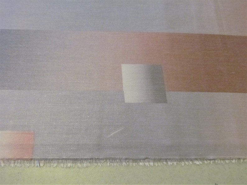 May include: A close-up of a fabric with a geometric pattern in shades of gray, pink, and brown. The fabric has a subtle shimmer and a textured surface.