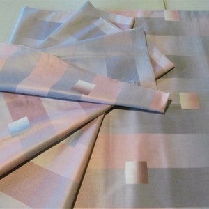 May include: A stack of fabric in a pink and gray plaid pattern. The fabric is soft and silky, and it would be perfect for making a dress, skirt, or blouse.