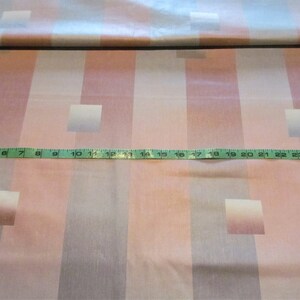 May include: A close-up of a pink and gray striped fabric with a repeating pattern of squares. A measuring tape is placed across the fabric, showing a measurement of 25 inches.
