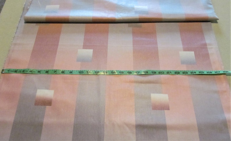 May include: A close-up of a pink and gray striped fabric with a repeating pattern of squares. A measuring tape is placed across the fabric, showing a measurement of 25 inches.