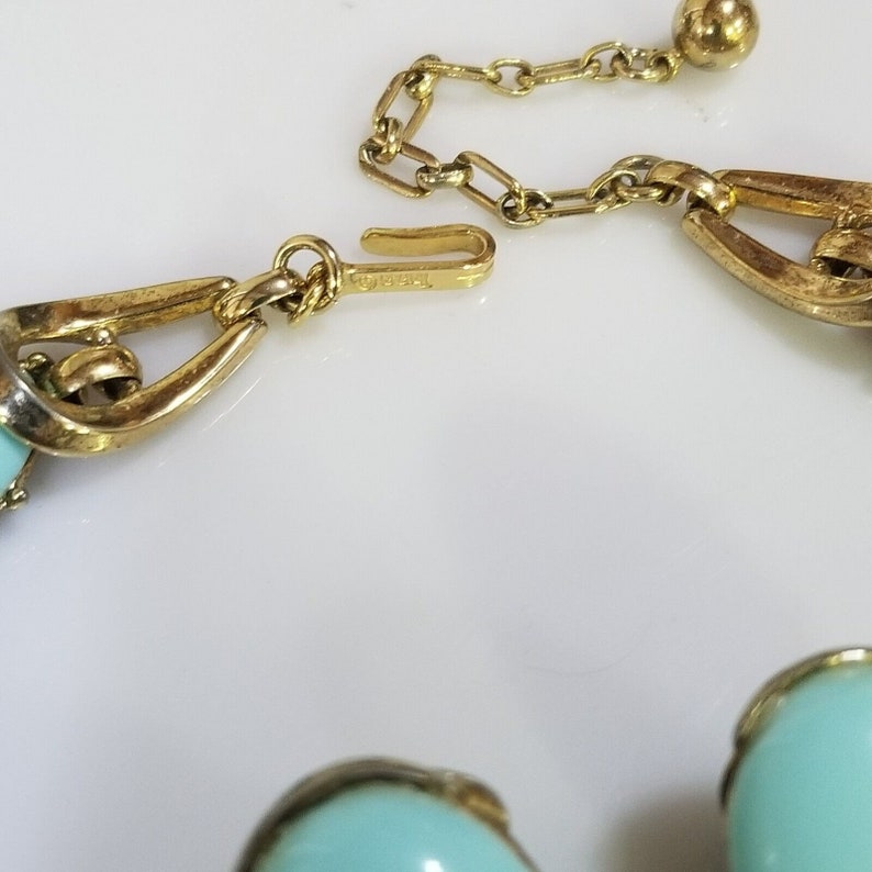 May include: Close-up of a vintage necklace with turquoise-colored beads and gold-tone metal chain and clasp. The necklace features a delicate chain and a hook clasp for secure fastening. The beads are a soft, pastel turquoise color.