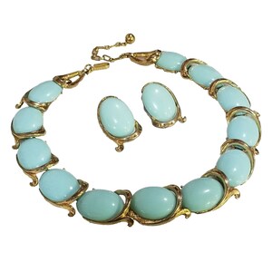 May include: A vintage jewelry set featuring a necklace and matching earrings. The necklace and earrings have oval, light blue stones set in gold-tone metal. The necklace is adjustable with a chain and clasp.