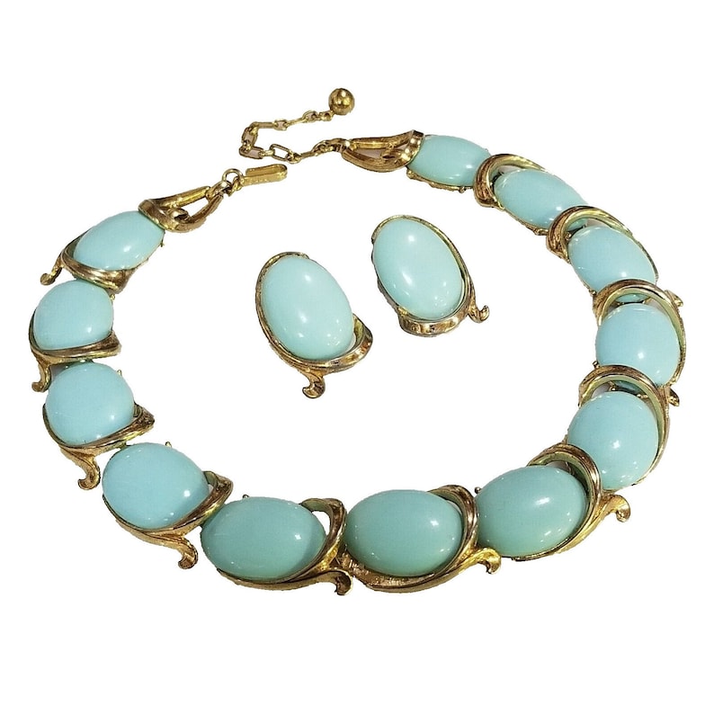 May include: A vintage jewelry set featuring a necklace and matching earrings. The necklace and earrings have oval, light blue stones set in gold-tone metal. The necklace is adjustable with a chain and clasp.