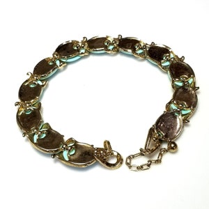 May include: A vintage gold-tone bracelet featuring oval-shaped links with a light blue center and decorative accents. The bracelet has a secure clasp and a small chain for adjusting the length. The jewelry is displayed on a white background.
