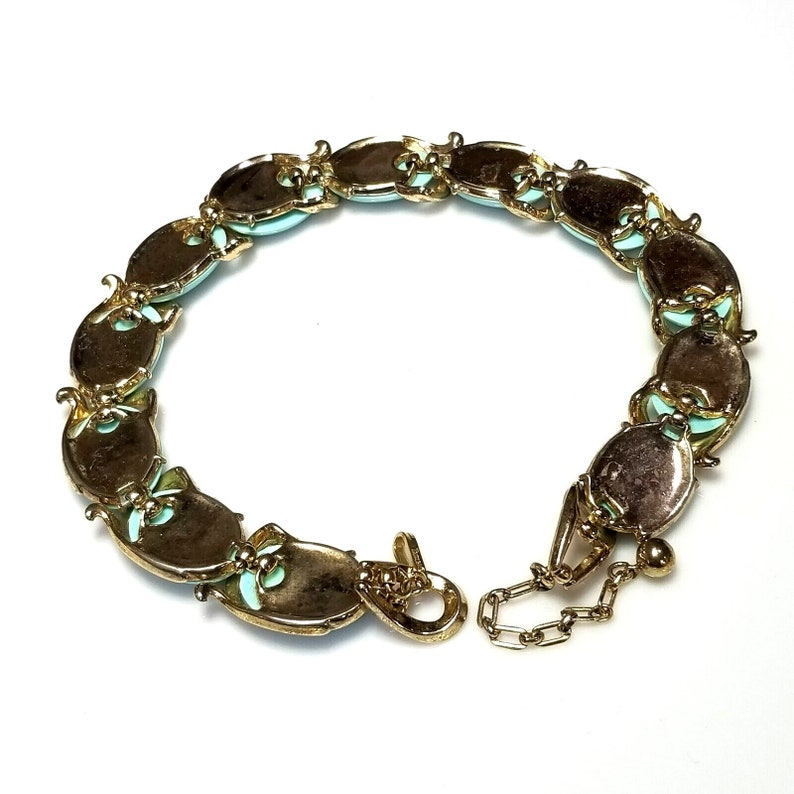 May include: A vintage gold-tone bracelet featuring oval-shaped links with a light blue center and decorative accents. The bracelet has a secure clasp and a small chain for adjusting the length. The jewelry is displayed on a white background.