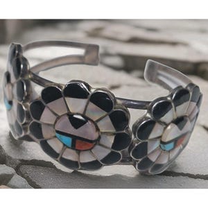 May include: A silver cuff bracelet with three flower motifs. Each flower has black, white, and iridescent petals, with a central mosaic of black, white, turquoise, and red. The bracelet is open-ended.