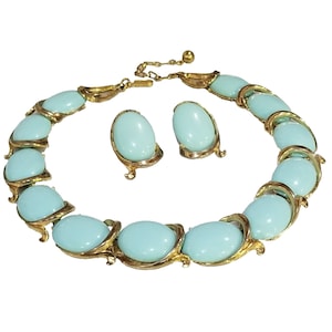 May include: A vintage jewelry set featuring a necklace and matching earrings. The necklace and earrings have oval, light blue stones set in gold-tone metal. The necklace is adjustable and has a hook closure.