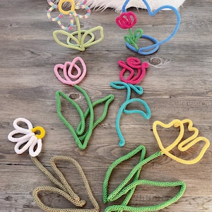 Puede incluir: Una colección de decoraciones de flores de ganchillo en varios colores, incluyendo rosa, amarillo, azul, verde y blanco. Las flores están dispuestas sobre una superficie de madera.