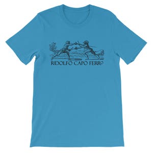 May include: A turquoise t-shirt with a black graphic of two fencers engaged in combat, and the words "RIDOLFO CAPO FERRO" underneath. The design is reminiscent of historical fencing, appealing to enthusiasts of historical combat.
