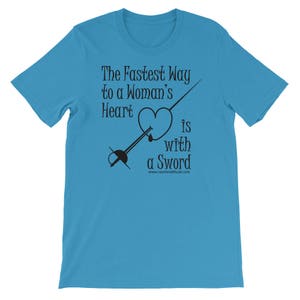 May include: A turquoise blue t-shirt with a black graphic design of a sword piercing a heart. The text reads "The Fastest Way to a Woman's Heart is with a Sword" and "www.cavalierattitude.com".