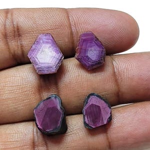 Könnte beinhalten: Vier facettierte Edelsteine in Lila und Schwarz. Die Edelsteine sind in hexagonaler Form geschliffen und haben eine dunkelviolette Farbe mit schwarzen Kanten.