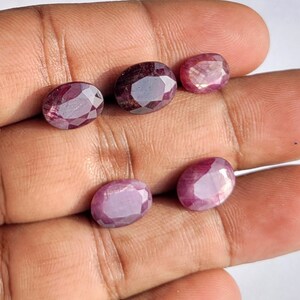 Puede incluir: Cinco piedras preciosas de forma ovalada en varios tonos de rosa y rojo. Las piedras preciosas están dispuestas en una fila sobre una mano.