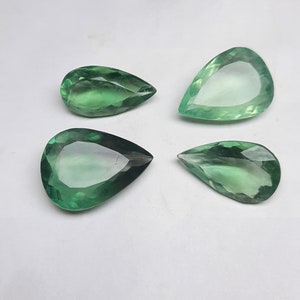 May include: Four pear-shaped green gemstones on a white background. The gemstones are faceted and have a translucent appearance.