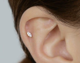 May include: A close-up of a person's ear with two different earrings. The first earring is a small, marquise-shaped diamond stud. The second earring is a row of three small, round diamond studs.