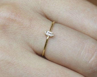 May include: A delicate gold ring with a small, rectangular, clear gemstone.