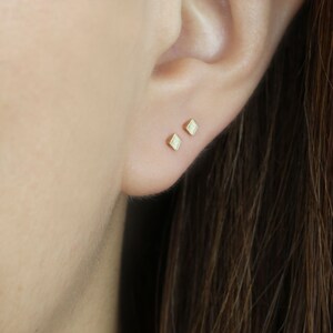 May include: A pair of small, square-shaped gold earrings with a textured surface.