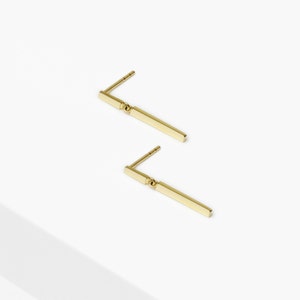 May include: A pair of gold bar earrings with a small ball accent. The earrings are simple and elegant.