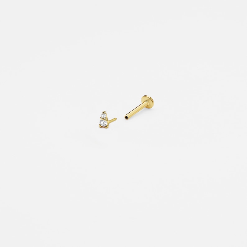 May include: A gold nose stud with two small clear gemstones set in a triangle shape.