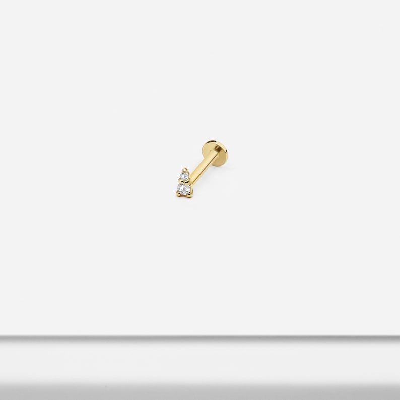 May include: Gold barbell earring with two small clear diamonds.