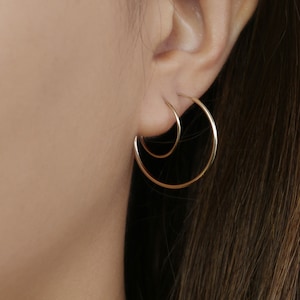 Puede incluir: Un par de pendientes de aro de oro, uno ligeramente más grande que el otro, usados en la oreja.