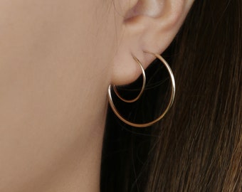May include: A pair of gold hoop earrings, one slightly larger than the other, worn in a person's ear.