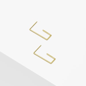 May include: A pair of gold-toned open hoop earrings. The earrings are made of a thin, rectangular wire.