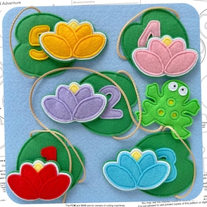 Könnte beinhalten: Ein Filz-Bastelset für Kinder mit einem Frosch, Seerosen und Zahlen. Das Set enthält einen grünen Frosch, fünf Seerosen mit den Zahlen 1-5 und gelbe, rosa, lila und blaue Blumen. Die Seerosen sind grün mit einem weißen Umriss. Das Set ist für Kinder konzipiert, um Zahlen und Farben zu lernen.