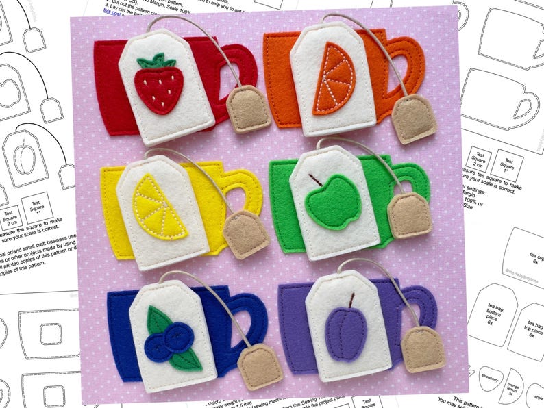 May include: A felt craft featuring six colorful tea cup and tea bag sets. Each tea bag has a different fruit design: strawberry, orange, lemon, apple, blueberry, and plum. The cups are red, orange, yellow, green, blue, and purple.