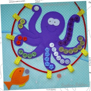 Könnte beinhalten: Ein lilafarbener Filz-Oktopus mit acht Tentakeln, jeder mit einer Reihe bunter Knöpfe. Der Oktopus befindet sich auf einem blauen Hintergrund mit weißen Punkten. Es gibt eine rote Schnur, die an den Oktopus befestigt ist, und einen gelben Filzfisch mit offenem Maul.