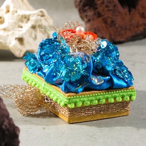 Decoratieve rechthoekige kartonnen doos, grijze binnenkant en gouden buitenkant met glitterblauwe stof, zalmbloem en vlechtwerk