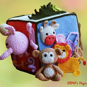 May include: A colorful, crocheted cube toy featuring various animal figures. The cube has a red, blue, and green design, with a crocheted elephant, cow, monkey, and lion attached. The toy is designed for children.