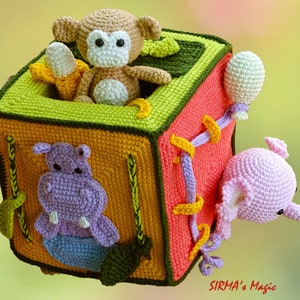 May include: A handmade crochet cube toy featuring a monkey with a banana, a hippo, and an elephant. The cube is multi-colored with green, orange, yellow, and pink sections. The toy has a whimsical design, perfect for children.