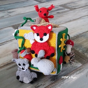 May include: A colourful crocheted cube toy featuring various animal characters, including a fox, rabbit, squirrel, and hedgehog. The cube has different textures and colours, making it a fun and engaging toy for children.
