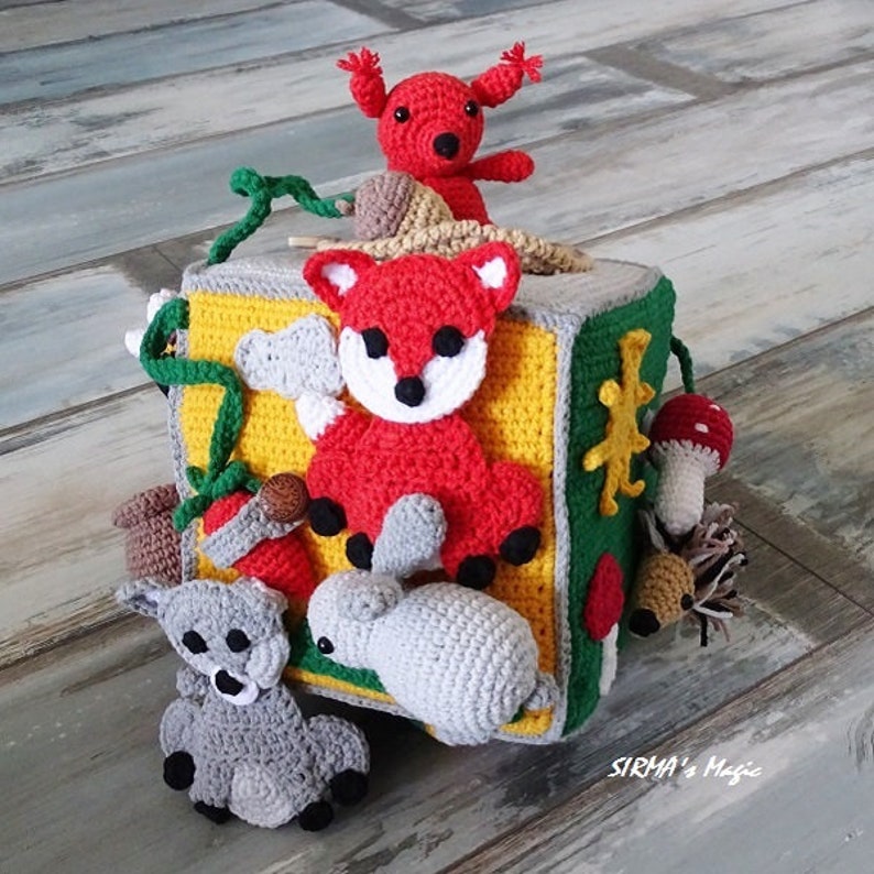 May include: A colourful crocheted cube toy featuring various animal characters, including a fox, rabbit, squirrel, and hedgehog. The cube has different textures and colours, making it a fun and engaging toy for children.