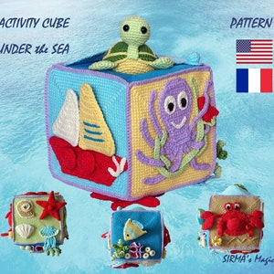 May include: A crocheted activity cube with a sea theme. The cube has six sides, each with a different sea creature or object. The sides feature a sailboat, an octopus, a starfish, a crab, a fish, and a turtle. The cube is made in bright colors and is perfect for a child's playroom.