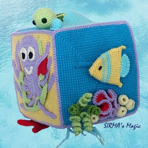 May include: A crocheted cube toy with different ocean-themed animals on each side. The cube features a purple octopus, a yellow fish, a green turtle, and coral. The cube is made of soft yarn and is perfect for babies and toddlers.