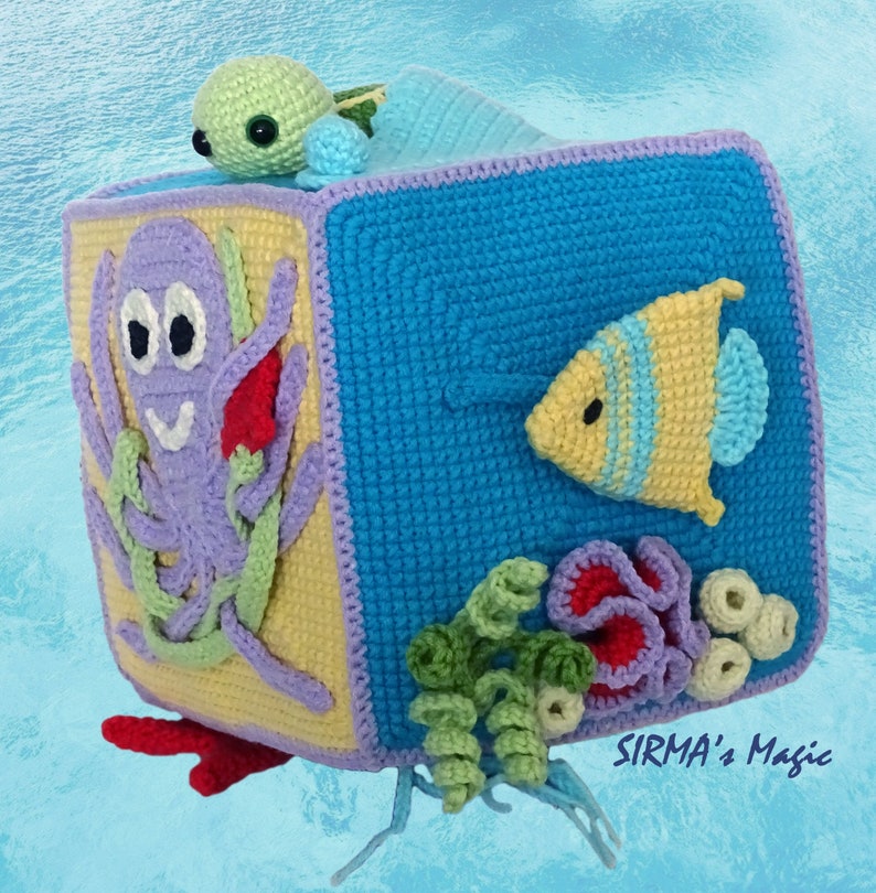 May include: A crocheted cube toy with different ocean-themed animals on each side. The cube features a purple octopus, a yellow fish, a green turtle, and coral. The cube is made of soft yarn and is perfect for babies and toddlers.