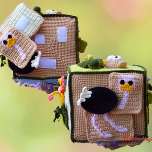 May include: Handmade crochet sensory cube with an ostrich theme. The cube is tan, green, and white, with a variety of textures and interactive elements. Features include a small square with an ostrich design, a black oval, and a white rectangle.