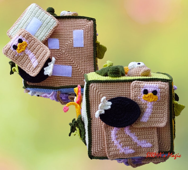 May include: Handmade crochet sensory cube with an ostrich theme. The cube is tan, green, and white, with a variety of textures and interactive elements. Features include a small square with an ostrich design, a black oval, and a white rectangle.