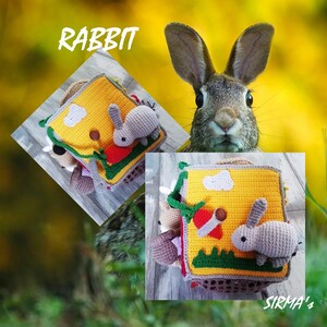 May include: A yellow, green and brown crocheted baby toy with a rabbit on the front. The toy is shaped like a book and has a variety of textures. The text "RABBIT" is visible in the image.