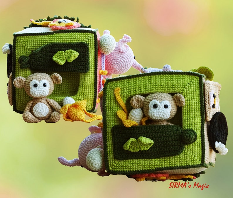 May include: A handmade crochet activity cube for babies, featuring a green and brown color scheme. The cube has various interactive elements, including a monkey, banana, and other animal figures. The design is soft and colorful, perfect for sensory play.