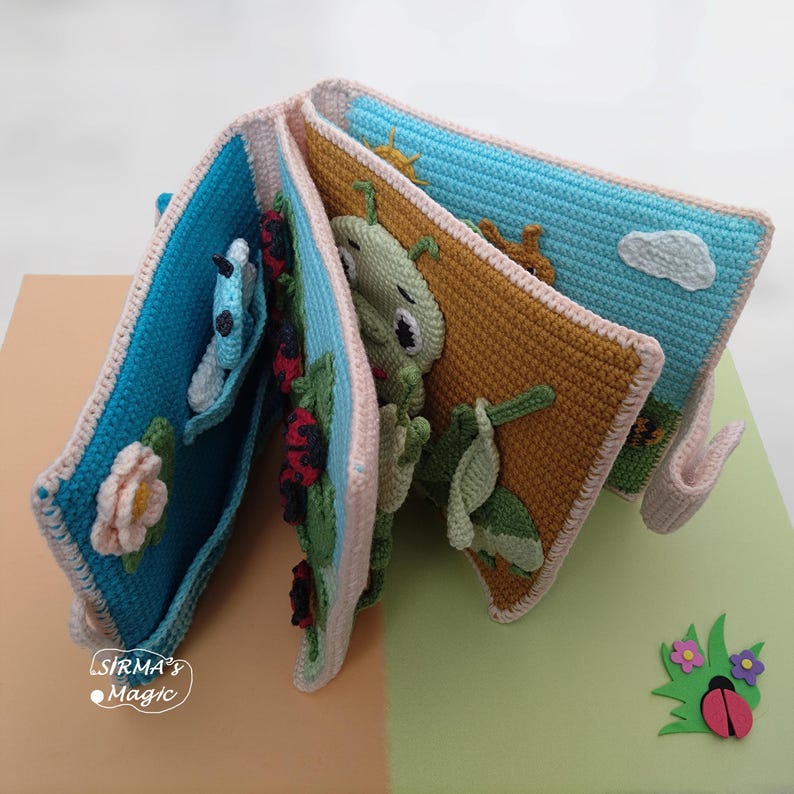 May include: A handmade crochet book with colorful pages featuring a butterfly, ladybugs, a caterpillar, and a sun. The book has a blue, pink, and brown color scheme, with the text "SIRMA's Magic" on the bottom left.
