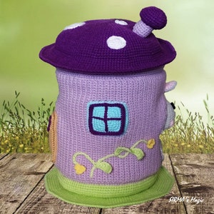 May include: A crocheted mushroom-shaped toy storage bin with a purple top, a lavender body, and a green base. The bin has a window and vines with yellow flowers.
