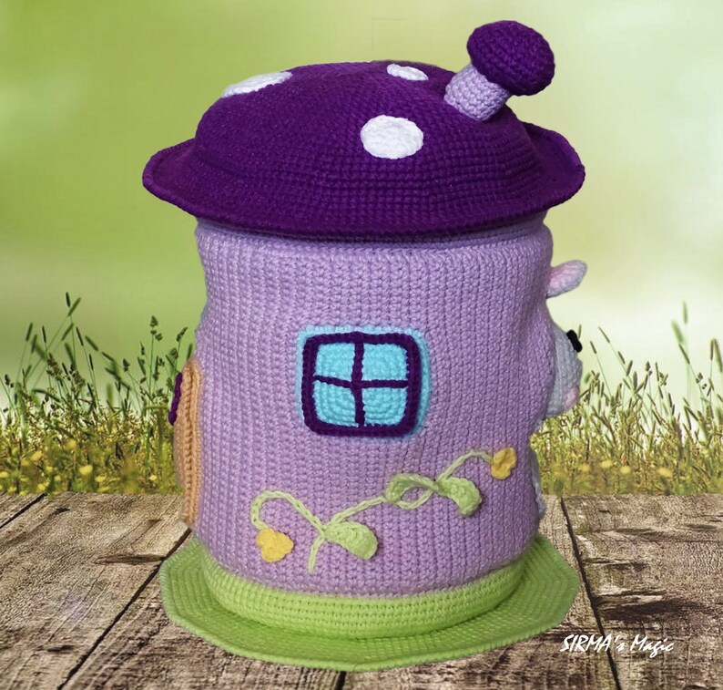 May include: A crocheted mushroom-shaped toy storage bin with a purple top, a lavender body, and a green base. The bin has a window and vines with yellow flowers.